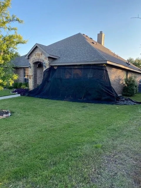 Suburban house with a black tarp covering the front exterior and a green lawn in the foreground
