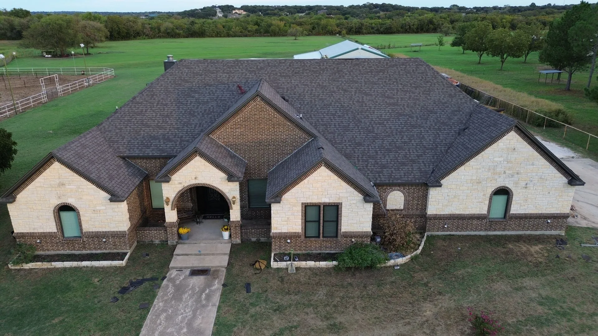 Large stone house with dark roof, arched entryway, and front walkway in a green rural setting
