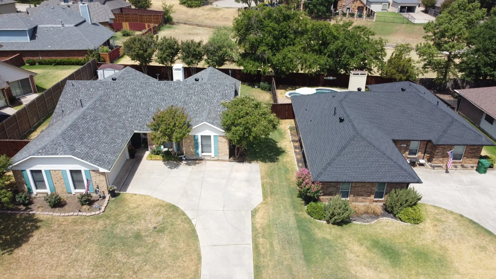 Aerial view of two suburban houses with driveways, lawns, and trees on a sunny day
