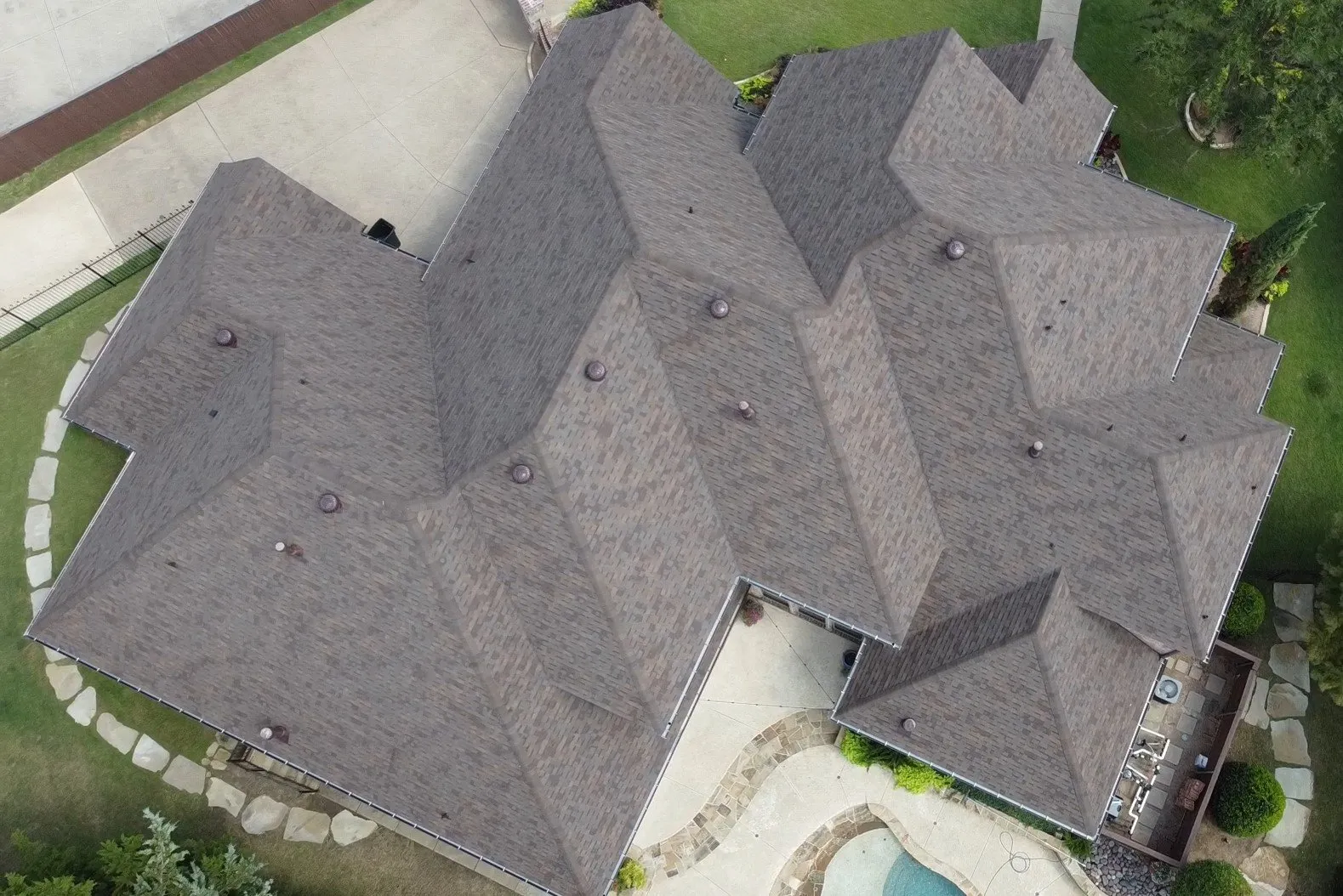Aerial view of a large gray-shingled house with multiple gables and a backyard pool.