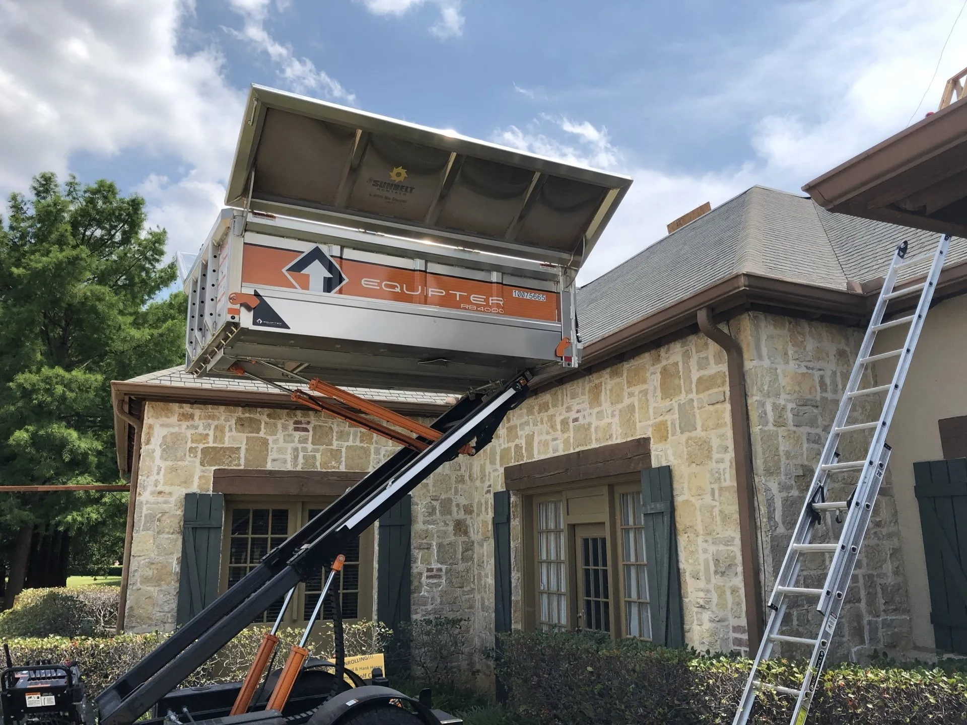 Stone house with roof repair lift and ladder under a partly open roof, outdoors in daylight