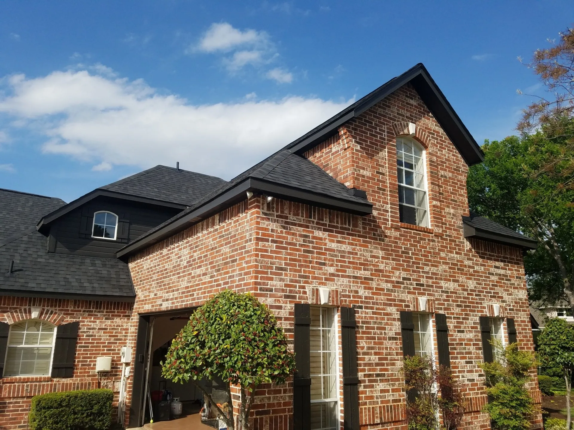 Brick house with black roof and dormer windows under a blue sky