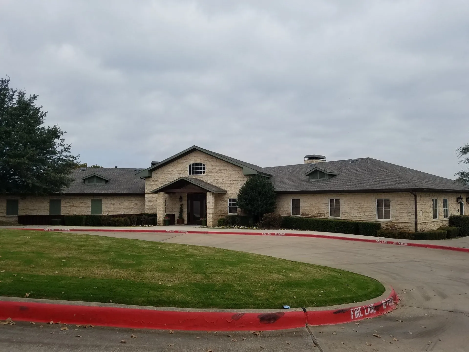 Single-story stone building with a central entrance and curved driveway under a cloudy sky